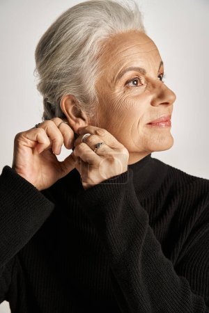happy middle aged business woman in elegant attire wearing hoop earrings on grey background