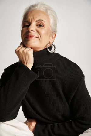 Porträt einer glücklichen Geschäftsfrau mittleren Alters in eleganter Kleidung und Reifrohren auf grauem Hintergrund