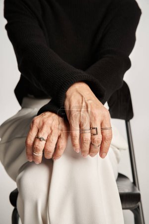 cropped middle aged business woman in smart casual attire and rings on fingers sitting on chair