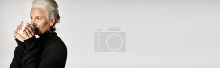 Téléchargez les photos : Heureuse femme d'âge moyen en pull col roulé noir tenant une tasse de café sur fond gris, bannière - en image libre de droit