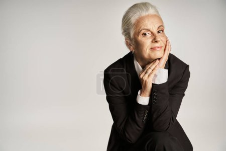 hermosa y gris mujer de mediana edad en traje elegante posando sobre fondo gris