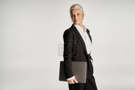 beautiful and grey haired middle aged woman in elegant attire posing on grey background