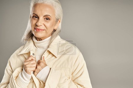 Téléchargez les photos : Belle et grise femme d'âge moyen en tenue élégante posant sur fond gris - en image libre de droit