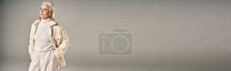 Téléchargez les photos : Belle et grise femme d'âge moyen en tenue élégante posant sur fond gris - en image libre de droit