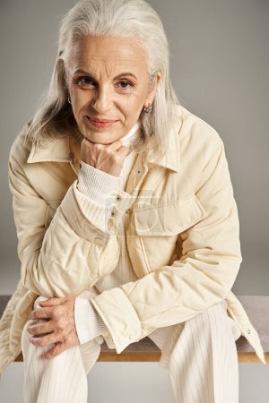 schöne und grauhaarige Frau mittleren Alters in eleganter Kleidung posiert auf grauem Hintergrund