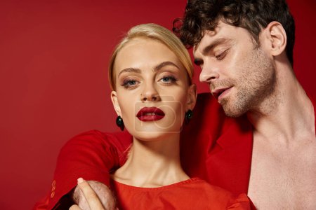 schöner Mann legt Hand um den Hals einer attraktiven blonden Frau mit roten Lippen vor lebendigem Hintergrund