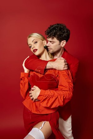 schöner Mann umarmt blonde Frau mit roten Lippen auf lebendigem Hintergrund, Valentinstag Mode