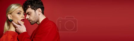 handsome man touching face of beautiful blonde woman with red lips on vibrant background, banner