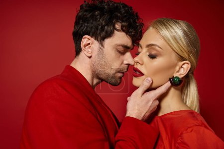 handsome man touching face of beautiful blonde woman with red lips on vibrant background, fashion