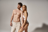 shirtless man with muscular body holding hand of blonde woman on grey background, sexy couple mug #689989838