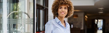 Smartly dressed and happy african american woman with curly hair standing in hotel lobby, banner