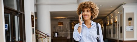 happy african american woman having phone call while walking in hotel lobby, horizontal banner