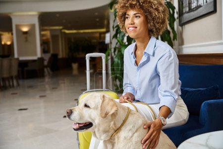 glücklicher Reisender wartet auf Check-in mit Labrador im haustierfreundlichen Hotel, schwarze Frau mit Hund