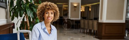 happy african american woman with curly hair waiting for check in hotel lobby, horizontal banner