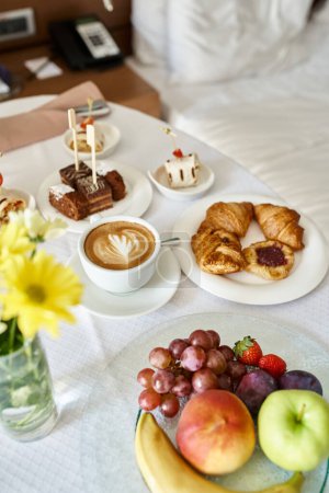 Hotel room service with fresh cappuccino and a variety of breakfast food, croissants and fruits