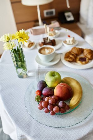 Hotel room service with fresh cappuccino and a variety of breakfast food, flowers and fruits