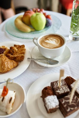 Hotel room service with fresh cup of cappuccino and variety of food for breakfast, cakes and fruits