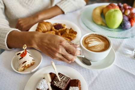 cropped shot of african american woman enjoying cappuccino and pastries with room service in a hotel