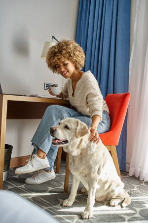 mujer afroamericana disfruta del café y trabaja remotamente cerca de su labrador en un hotel que acepta mascotas