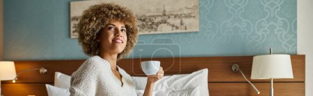 Banner der glücklichen afrikanisch-amerikanischen Frau, die Kaffee genießt, während sie auf dem Hotelbett sitzt, Wochenendausflug