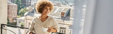 verträumte junge afrikanisch-amerikanische Frau steht mit Tasse Kaffee auf Hotelbalkon, Reisebanner