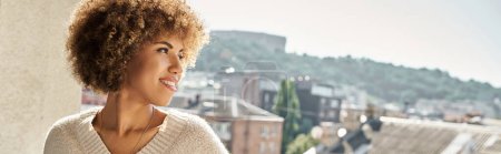 glückliche junge afrikanisch-amerikanische Frau auf sonnigem Hotelbalkon mit Blick auf die Stadt, Reisebanner
