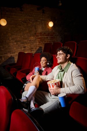 Téléchargez les photos : Gai divers couple élégant en tenue rétro souriant et regarder des films sur la date dans le cinéma - en image libre de droit