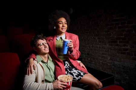 freudig vielfältiges Paar in Retro-Kleidung, die gemeinsam Film auf Datum im Kino, Valentinstag