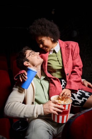 amante diversa pareja en traje retro sonriendo el uno al otro mientras que en la fecha en el cine, Día de San Valentín