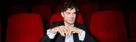 handsome elegant man with dapper style sitting on red cinema chairs and looking away, banner