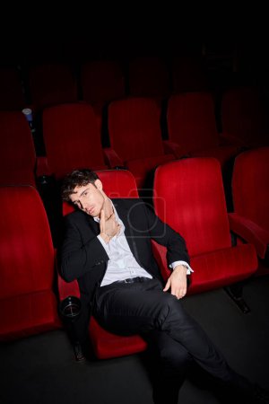 appealing elegant male model with dapper style enjoying movie at cinema and looking at camera