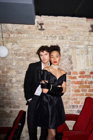 attraktives multiethnisches Paar in Abendkleidern posiert zusammen und schaut beim Date in die Kamera