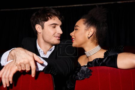 Foto de Atractivo joven pareja multirracial en trajes negros sonriendo el uno al otro con amor, Día de San Valentín - Imagen libre de derechos