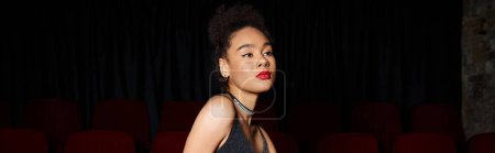 Photo for Beautiful young african american woman in black dress posing at cinema and looking away, banner - Royalty Free Image