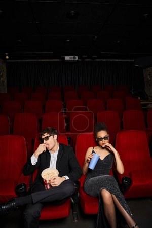 Téléchargez les photos : Beau couple diversifié dans des tenues de soirée élégantes avec des lunettes 3D regarder le film sur la date - en image libre de droit