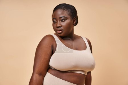 Photo for Plus size African American woman in beige undergarments posing thoughtfully on beige background - Royalty Free Image
