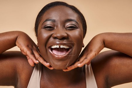 Photo for Cheerful plus size african american woman smiling with hands near her face on beige background - Royalty Free Image