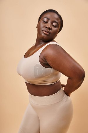 junge plus size afrikanisch-amerikanische Frau in Unterwäsche posiert auf beigem Hintergrund, Körper positiv