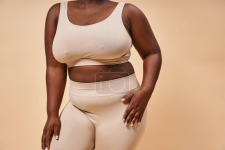 cropped plus size african american woman in underwear posing on beige background, body positive