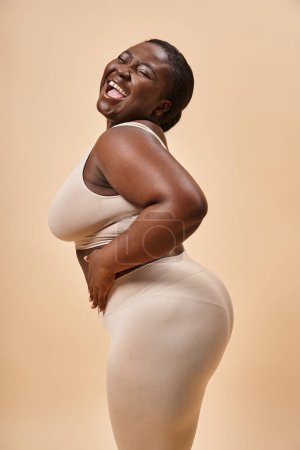 Photo for Cheerful plus size african american woman posing against matching backdrop, body positive - Royalty Free Image