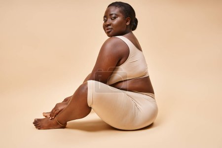 Body positive, plus size afrikanisch-amerikanische Frau in Unterwäsche posiert vor beigem Hintergrund