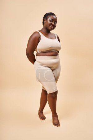 mujer feliz más tamaño en ropa interior beige posando en el estudio, el cuerpo positivo y la autoestima