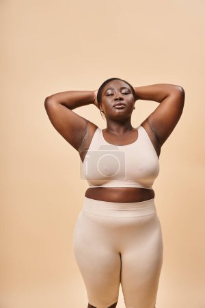 Photo for Calm plus size woman in beige underwear posing with hands near head, body positive and self esteem - Royalty Free Image