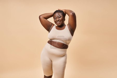 Photo for Happy plus size woman in beige underwear posing with hands near head, body positive and self esteem - Royalty Free Image