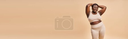 Téléchargez les photos : Heureux plus taille femme en sous-vêtements beige posant avec les mains près de la tête, corps bannière positive - en image libre de droit