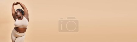 Téléchargez les photos : Bannière de femme heureuse de taille plus en sous-vêtements beige posant avec les mains levées, corps positif - en image libre de droit