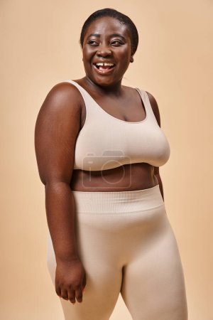 Photo for Joyful plus size woman in beige underwear laughing and looking away, body positive and self esteem - Royalty Free Image