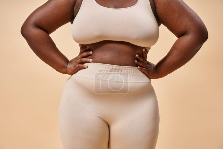 cropped plus size woman in underwear posing on beige backdrop, body positive and female empowerment
