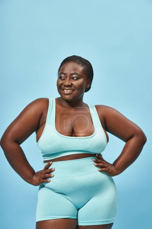 plus size african american woman in stylish active wear looking back and posing with hands on hips