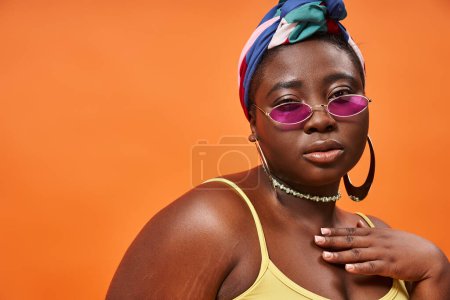 Photo pour Fashion-forward et taille plus femme afro-américaine en foulard et lunettes de soleil tendance sur orange - image libre de droit